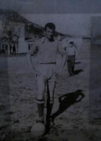 Ασπρόμαυρη φωτογραφία ενός άντρα, του Γιώργου, παίζοντας μπάλα σε τοπική ομάδα. Είναι ντυμένος με καθημερινά ρούχα. 